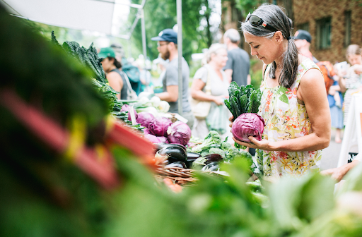 A woman holding cabbage and kale at a farmers market.